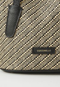 Black and cream woven handbag featuring a textured surface, diagonal pattern, and a black leather accent with embossed logo.