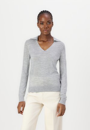 Pull en gris à manches longues avec un col en V et un col. Tissu tricot léger avec une texture subtile, associé à un pantalon large crème.