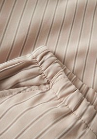 Tissu beige clair avec de fines rayures verticales, doté d'une taille élastique et d'une texture froncée pour le confort et l'ajustement.
