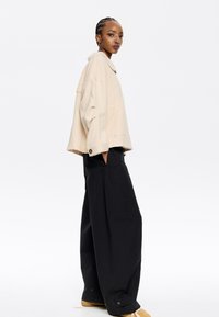 Giacca beige oversize con collo e tasca frontale. Abbinata a pantaloni neri a vestibilità ampia e scarpe color beige, che evidenziano una silhouette rilassata.