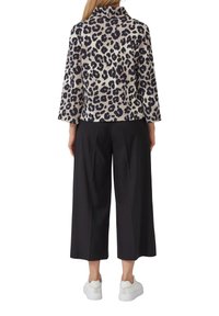 Giacca con stampa leopardata e colletto finto, abbinata a pantaloni neri a gamba larga e sneakers bianche, creando un look monocromatico a contrasto.