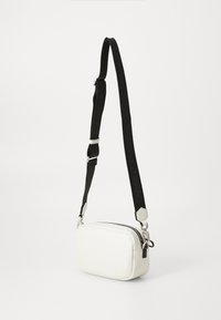 White leather crossbody bag with a rectangular shape, zip closure, and black adjustable strap featuring a logo. Silver-toned hardware accents.