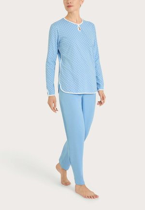 Donna che cammina a piedi nudi indossando una maglia a maniche lunghe azzurra a pois con rifiniture bianche e pantaloni blu tinta unita abbinati.