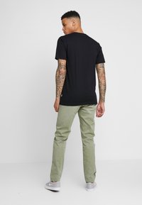 Černé bavlněné tričko s kulatým výstřihem, doplněné o světle zelené kalhoty. Model stojí a předvádí volnočasový outfit zezadu.