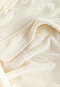 Miękki, kremowy materiał o prążkowanej fakturze, z delikatnymi fałdami i gładkim wykończeniem, idealny do odzieży lub dekoracji wnętrz.