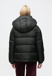 Sort dunjakke med hætte, der har et quiltet design og elastiske manchetter, vist bagfra, kombineret med bordeaux bukser.