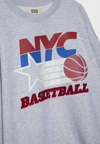Sweat gris avec texte NYC rouge et bleu, étoile blanche, graphique de basketball et mot « basketball » brodé en rouge sur le devant.