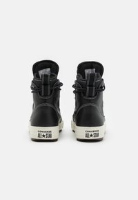 Svarta högskor i läder med vita snören, vadderad krage och gummisulor. Anmärkningsvärd branding på hälen och kontrasterande sömmar.