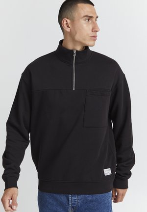 Sudadera negra con cuello de cremallera, con un bolsillo en el pecho, hecha de tejido suave, presenta mangas largas y un corte relajado.