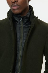 Õliverohelist villasegu mantel musta sisevoodriga, millel on kõrge krae, lukustus lukuga ja ees nupu detailid.