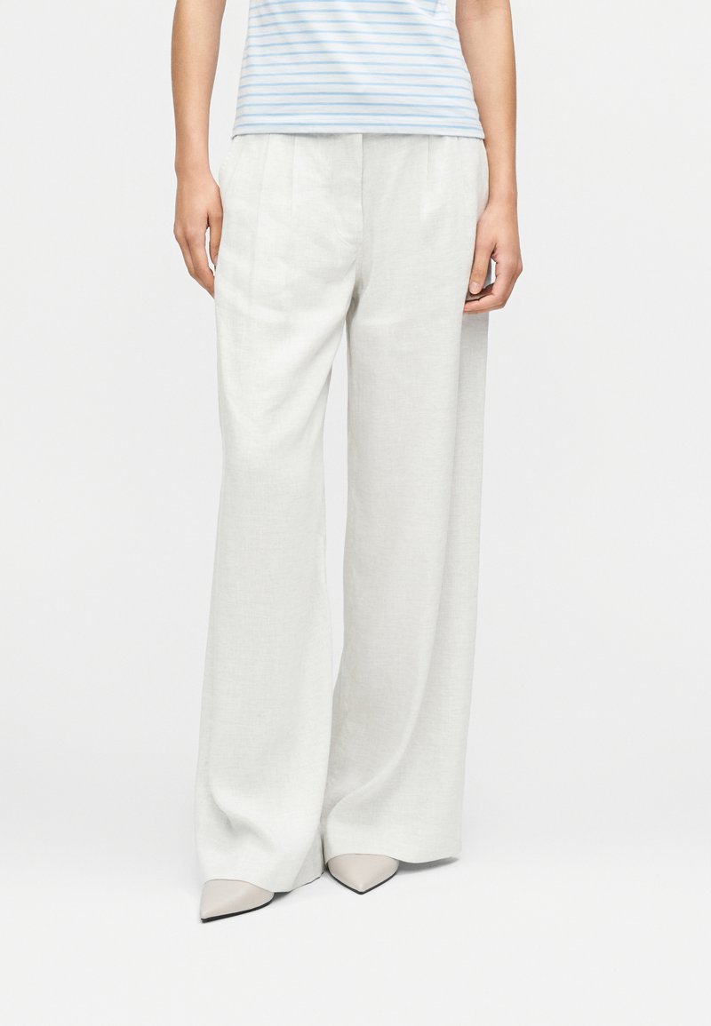 Φαρδιά παντελόνια από ελαφρύ λινό σε απαλό γκρι με διακριτική υφή και πιέτες. Συνδυασμένα με εφαρμοστή μπλούζα με μπλε και λευκές ρίγες και μπεζ μυτερά παπούτσια.