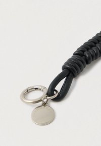 Černý kožený přívěsek na klíče s pletenou texturou, vybavený stříbrným kovovým kroužkem a kulatou visačkou s vyrytým nápisem „Kodaň“.