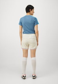 Zila sporta krekls ar īsām piedurknēm, krēma šorti ar krāsainiem svītrainiem akcentiem, baltas ceļgala garuma zeķes un melni ar sarkaniem sporta apaviem.