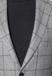 Szary marynarka w kratę z teksturowanej tkaniny, z czarnym golfem pod spodem. Marynarka ma klapowany kołnierz i pojedynczy guzik.