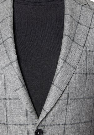 Szary marynarka w kratę z teksturowanej tkaniny, z czarnym golfem pod spodem. Marynarka ma klapowany kołnierz i pojedynczy guzik.