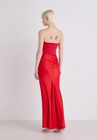 Rochie roșie din satin, fără bretele, cu un corset ajustat și fustă evazată. Are un fermoar la spate și o textură netedă. Accentuată cu o trenă subtire.