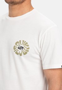 Bílý bavlněný tričko s kulatým, multikolorním logem a textem "Quicksilver" a grafickými prvky na levé části hrudi.