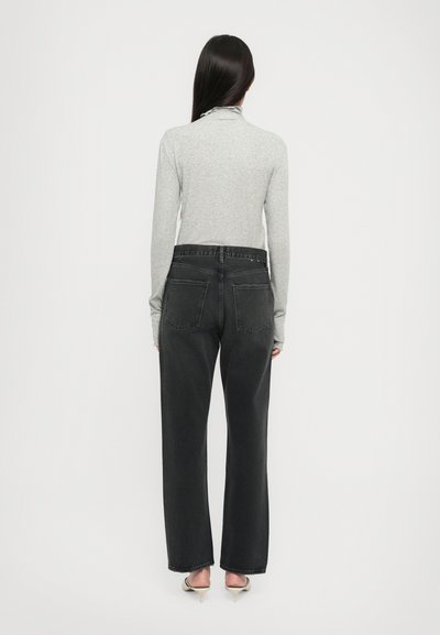 Graues Longsleeve-Oberteil kombiniert mit hochtaillierten schwarzen Jeans aus Denim, ausgestattet mit zwei Gesäßtaschen und geradem Beinverlauf, dazu spitze Absätze.