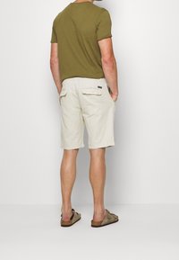 Kaki t-shirt med uppvikta ärmar, i kombination med beige cargo shorts med bakfickor. Bärs med bruna slip-in sandaler.