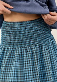 Jupe à carreaux bleus et noirs avec une taille smockée et un tissu texturé, présentant des sections froncées et une coupe évasée.