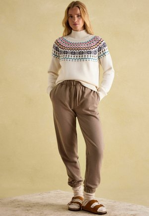 Knit sweater in cream with multicolored geometric patterns; paired with brown jogger pants and brown sandals with white accents.