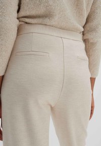 Pantalones texturizados beige con una cinturilla ajustada, que cuentan con dos bolsillos traseros con un borde sutil. Tela suave y elástica con una forma ajustada.