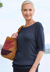 Navy-blaues Strickoberteil mit kurzen Ärmeln, getragen von einer Frau, kombiniert mit einer mehrfarbigen Gewebetasche mit orangefarbenen, rosa und lila Akzenten.