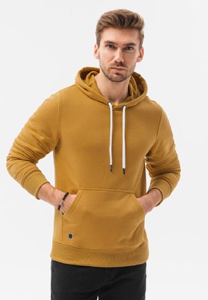 Żółta bluza z kapturem i sznureczkiem, z przednią kieszenią i ściągaczami przy rękawach. Nosi się z czarnymi spodniami. Gładka faktura, casualowy design.