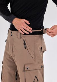 Beige broek met een ontspannen fit, voorzien van meerdere zakken, ritsdetails, een klittenbandsluiting in de taille en een logo op het been.