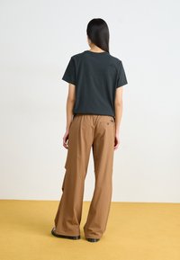 T-shirt noir en coton à encolure ronde, associé à un pantalon cargo marron ample avec des poches latérales et une taille froncée.