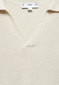 Helles beiges Strickpullover mit V-Ausschnitt und strukturierter Oberfläche. Das Etikett trägt MNG und weist auf Größe M hin (EUR, USA, MEX).