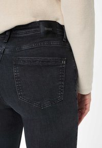 Jeans in denim neri con una forma aderente, dotati di una patch in pelle nera con logo, tasche posteriori e una consistenza morbida.
