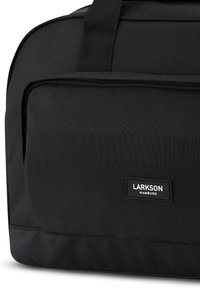 Fekete szövet utazótáska tartós szintetikus anyagból, amely téglalap alakú, elülső cipzáros zsebével és márkázott címkéjével rendelkezik.