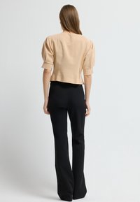 Beige cropped bluse med puffede ærmer, tekstureret stof og subtile metalliske detaljer, parret med sorte tætsiddende bukser.