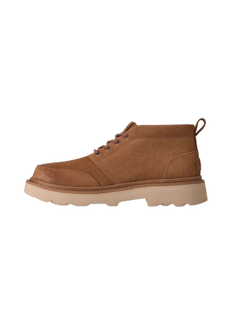 Bota de ante marrón con cordones hasta el tobillo, suela de goma gruesa beige y lengüeta en la parte posterior, vista lateral sobre fondo blanco.