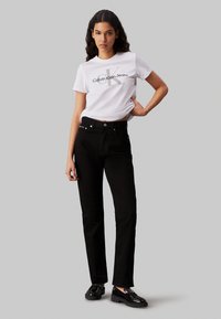 Vaqueros negros de pierna recta con herrajes plateados, con un diseño clásico. Combinados con una camiseta de cuello redondo blanca que muestra un logo.