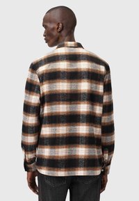 Rutig skjorta i svart, brunt och kräm med krage. Har en mjuk textur och långa ärmar med knäppte manschetter. Bakåtvy visas.