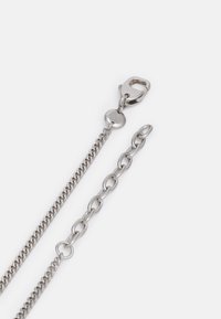Cadena de metal plateado con un diseño de eslabones planos. Cuenta con un broche para sujeción y una textura suave y pulida.