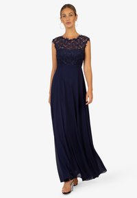 Abito da sera blu navy con corpino in pizzo, maniche a cappuccio e gonna fluida in chiffon. I dettagli trasparenti aggiungono un contrasto tattile.
