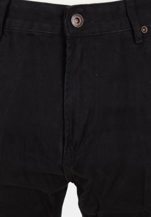 Primo piano di pantaloni di denim neri che mostrano la chiusura con bottone e gli passanti per cintura sulla vita.