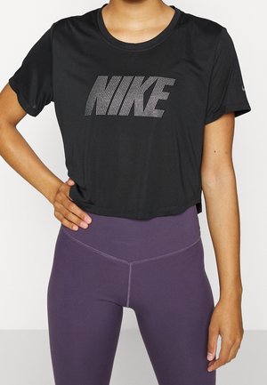 Maglietta cropped nera realizzata in tessuto liscio, con un grande logo Nike a pois sul davanti. Abbinata a leggings viola.