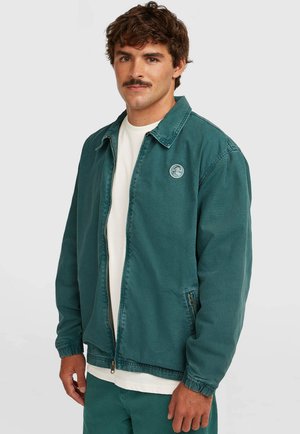 Havgrøn lynlåsjakke med krave, elastiske manchetter og sidelommer. Har en rund logopatch på venstre bryst.