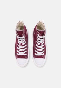 Para bordo wysokich trampków z kanwy z białymi gumowymi noskami, białymi sznurówkami i białymi podeszwami na jasnoszarym tle.