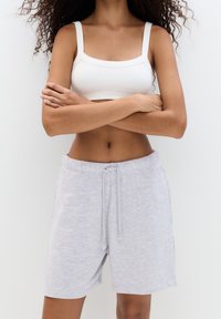 Bralette bianco a coste e pantaloni corti grigi chiari con coulisse realizzati in tessuto morbido. I pantaloni corti presentano un elastico in vita e tasche laterali.