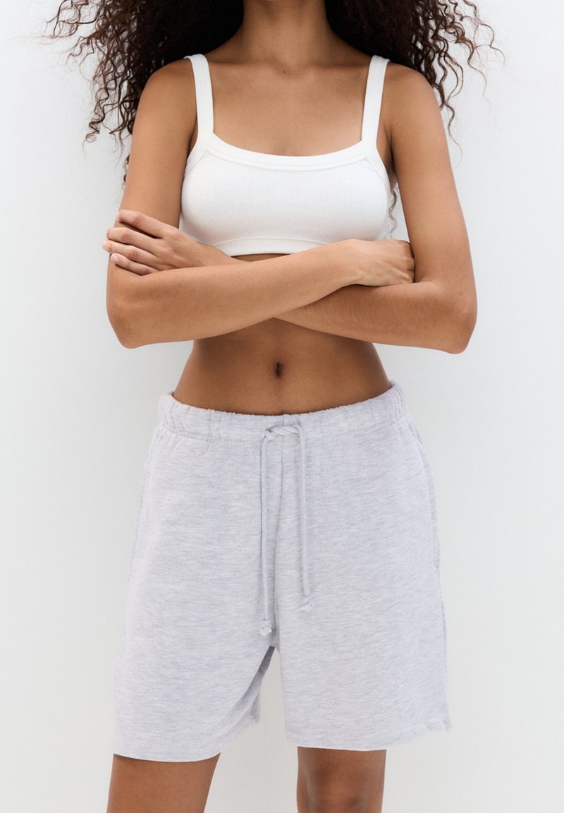 Bralette bianco a coste e pantaloni corti grigi chiari con coulisse realizzati in tessuto morbido. I pantaloni corti presentano un elastico in vita e tasche laterali.