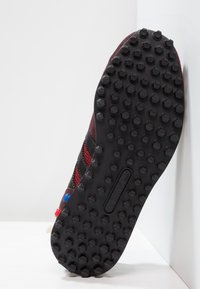 Svart och röd träningssko med en texturerad gummisula som har framträdande runda nubb för grepp och stabilitet.