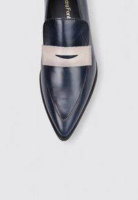 Zapato de cuero azul marino con puntera puntiaguda y correa beis con un detalle recortado en la parte media del pie, suela plana y acabado suave.