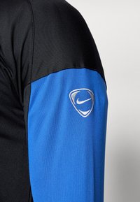 Black and blue athletic long sleeve top with a smooth texture, featuring a prominent silver Nike logo on the blue section of the sleeve.