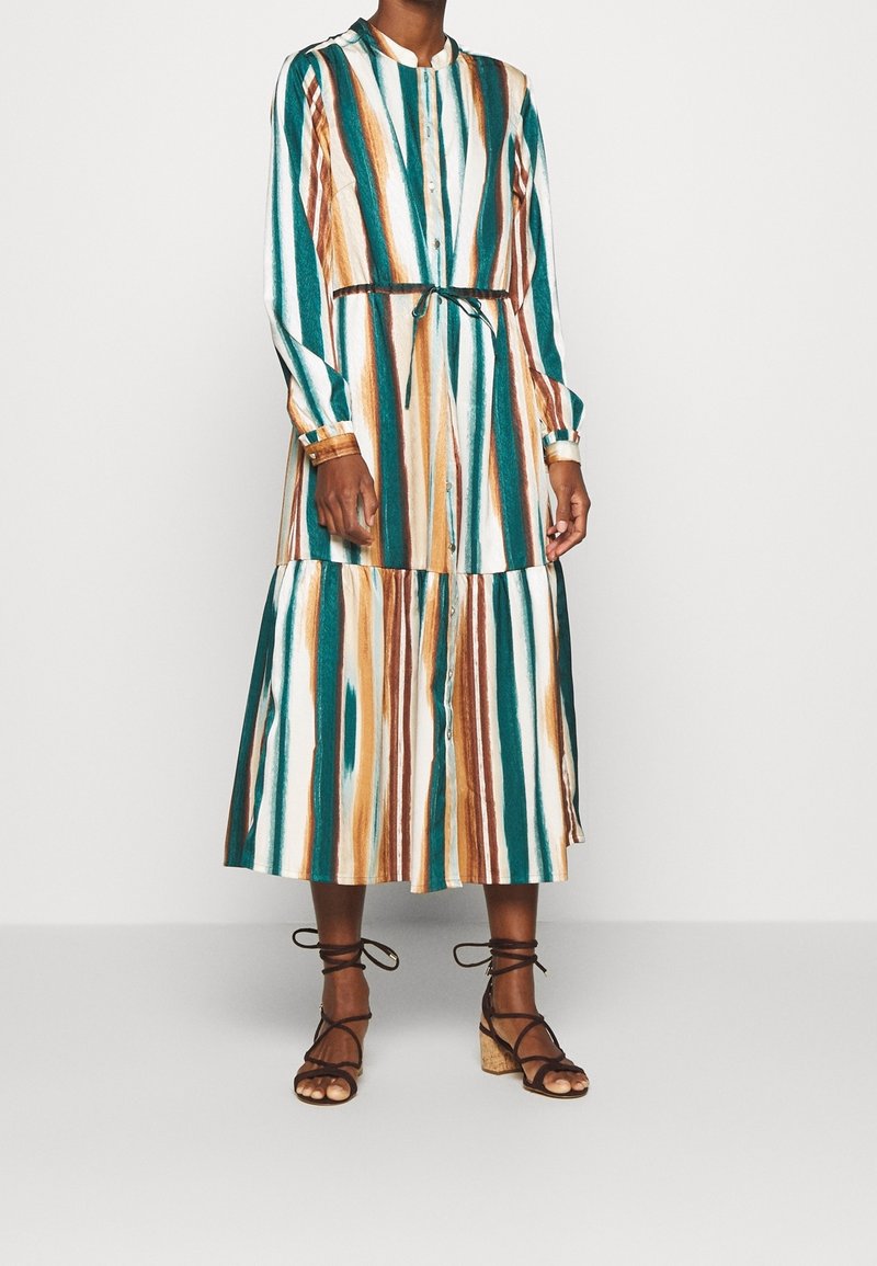 Abito a maniche lunghe a righe in teal, bianco e marrone. Presenta una chiusura con bottoni sul davanti, una vita arricciata con un nastro e un design a strati nella gonna.