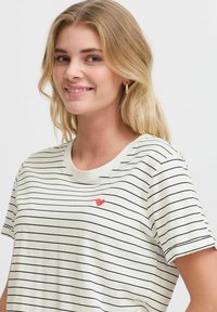 T-shirt rayé en crème clair avec des rayures noires, col rond, manches courtes et une petite broderie en forme de cœur rouge sur la poitrine.
